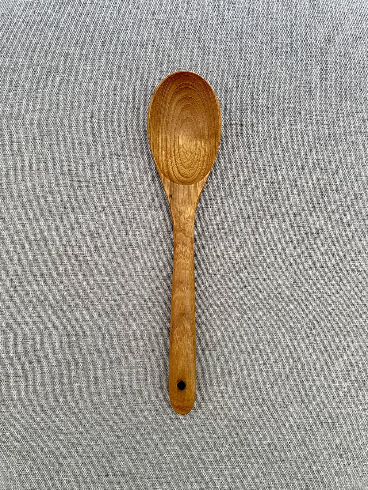 Handmade teak wood cooking spoon with deep bowl on grey linen