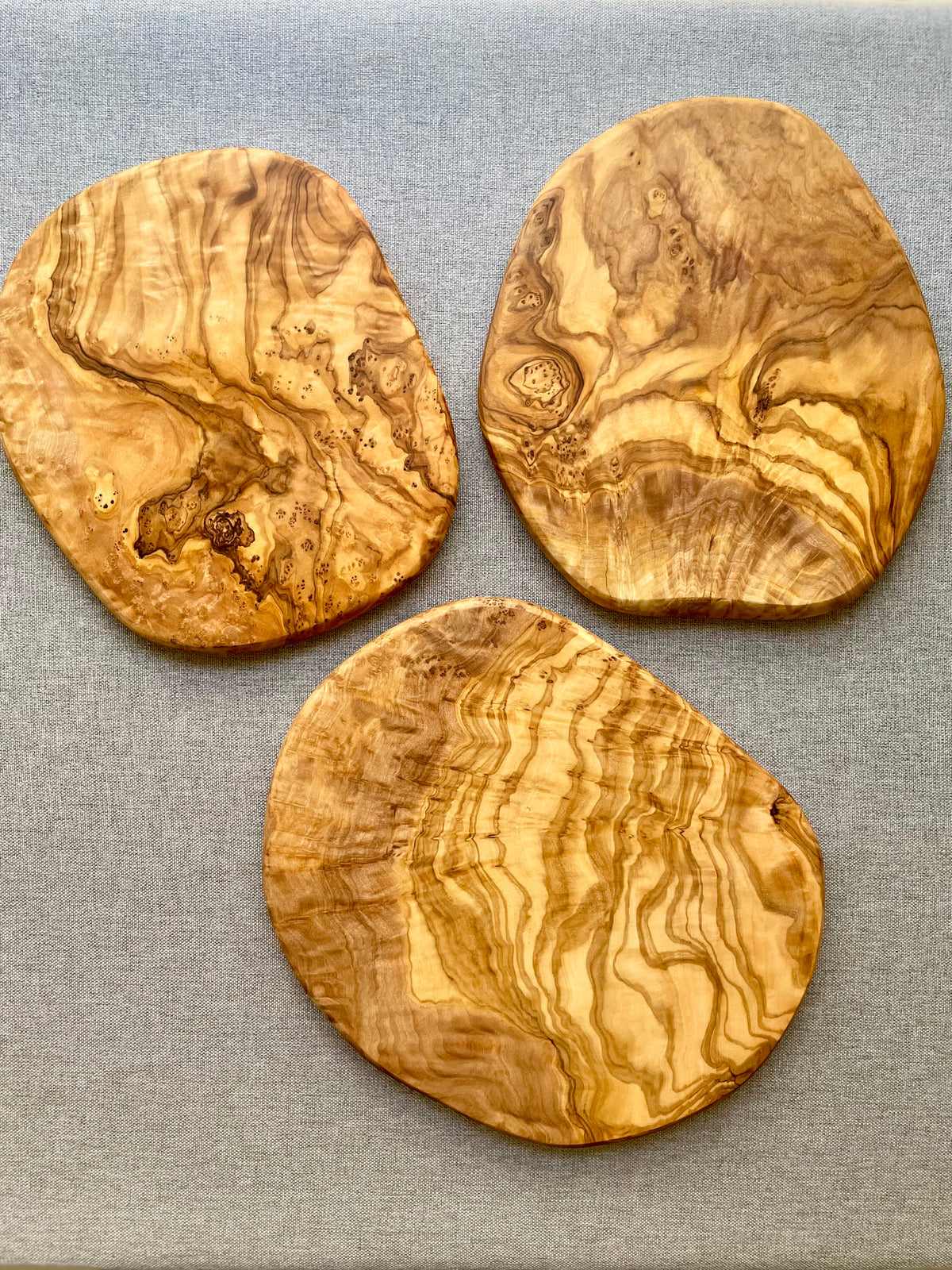 Close-up of a single round olive wood trivet with dramatic swirling grain on a gray fabric background - hand-made from natural olive wood.