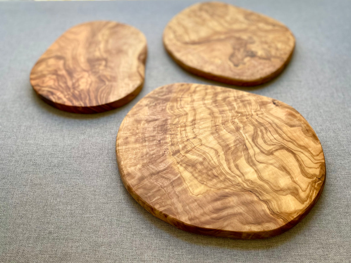 Round olive wood trivets with wavy grain on a gray fabric background - hand-made from natural olive wood, each one unique in size and shape.