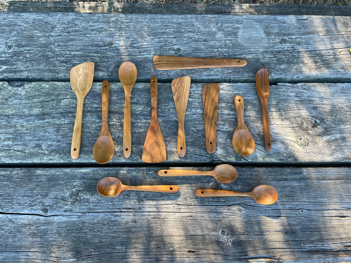 Twelve-piece teak wood kitchen utensil set on weathered wood