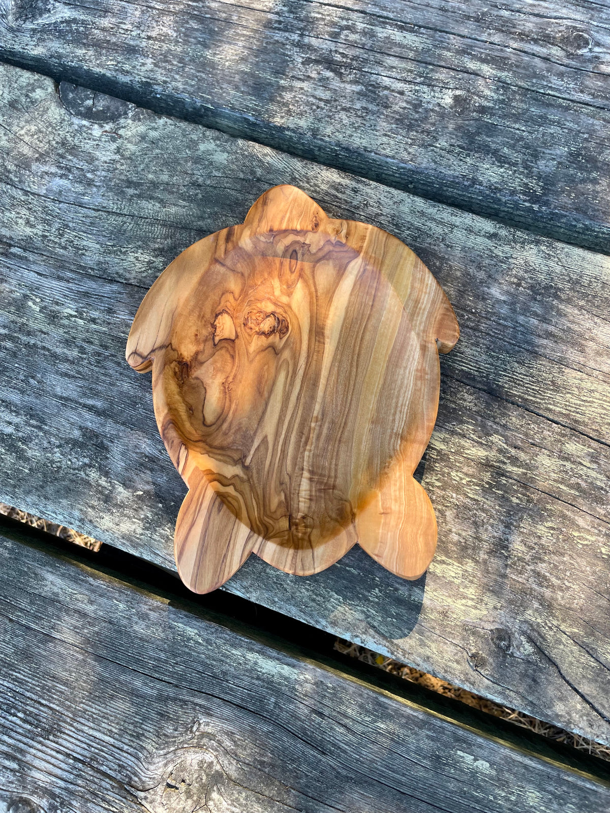 Olive wood turtle-shaped dish on weathered gray wood planks - hand-carved from natural olive wood with swirling grain.
