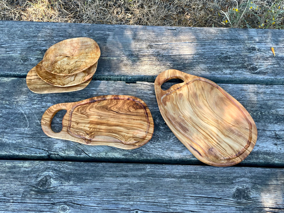 Three olive wood cutting and serving boards with carved handles and grooves on a weathered outdoor table - hand-made from natural olive wood, each with unique grain.