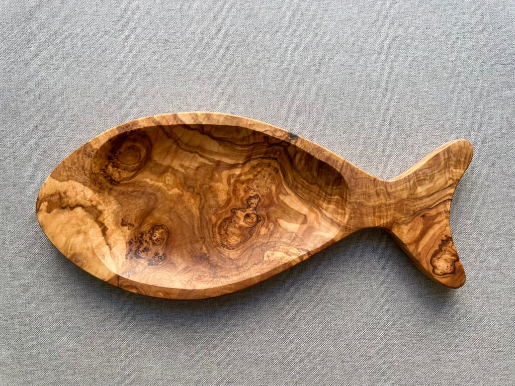 Olive wood fish-shaped serving dish on a gray fabric background - hand-carved individually from top-quality olive wood, perfect for snacks.