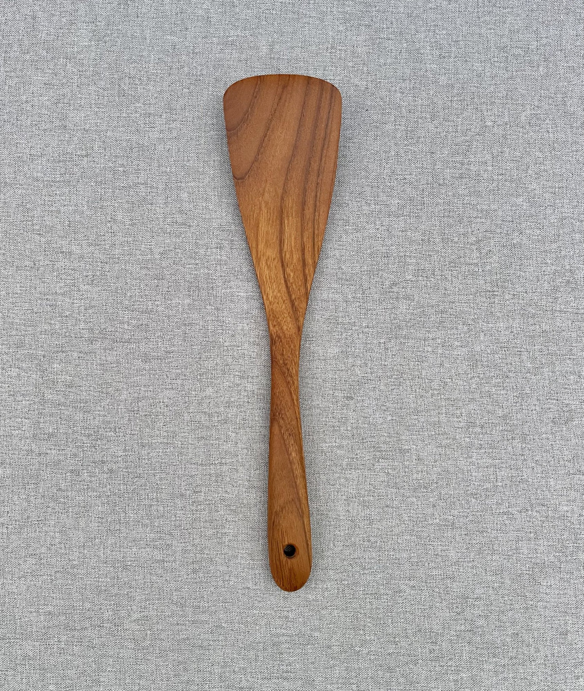 Handmade teak wood spatula with curved head on grey linen