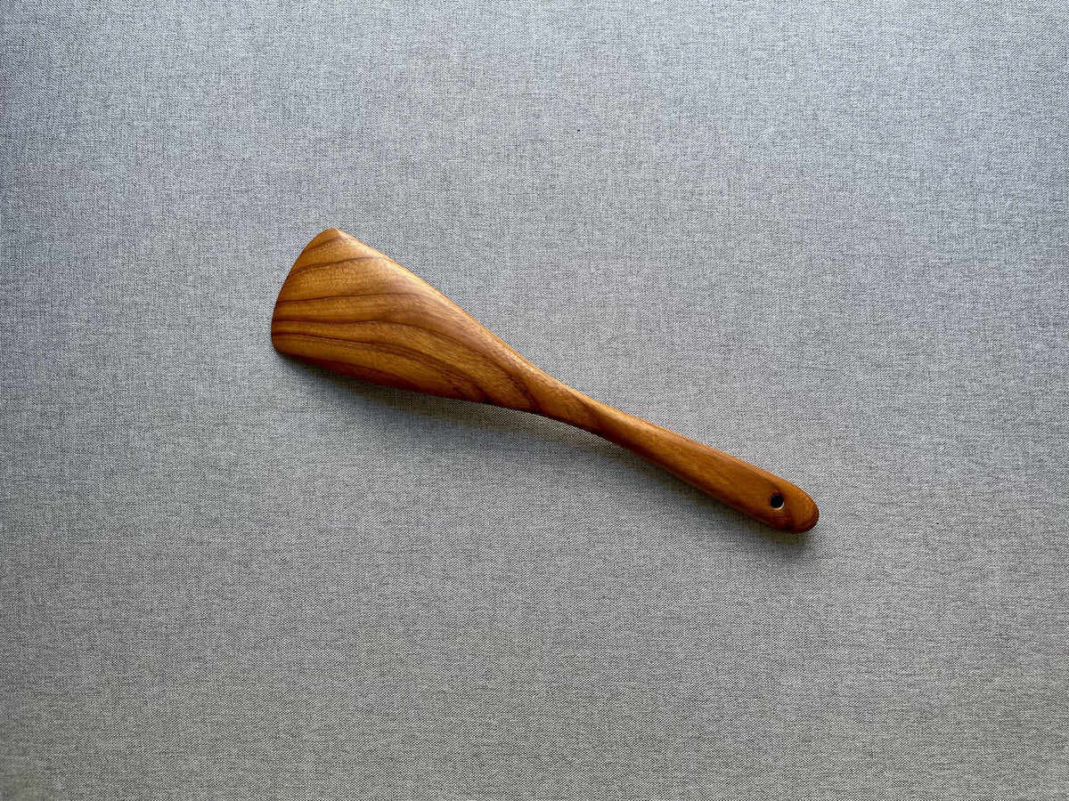 Teak wood kitchen spatula with golden grain, angled view